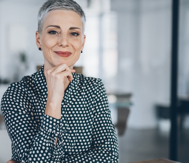 Frau in Bluse stützt sich auf dem Tisch auf und lächelt einen entspannt an.