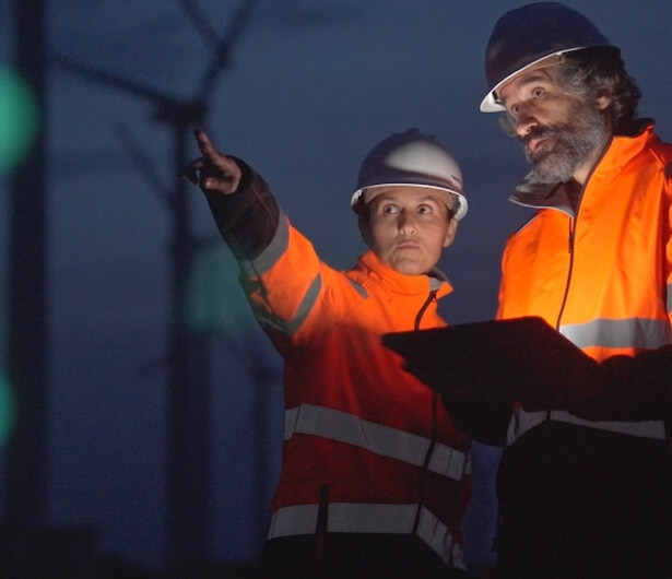 Zwei Männer stehen vor einem Windpark. Ein Techniker mit Tablet bei der Arbeit vor Ort, der einen digitalen Arbeitsauftrag oder eine Checkliste in der Flow360-Software ausfüllt.